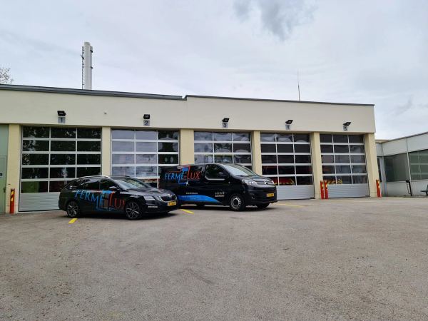 Feuerwache mit fünf verglasten Sektionaltoren und zwei davor geparkten Firmenfahrzeugen
