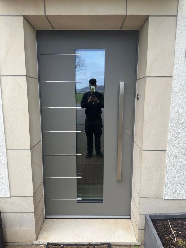 Graue Haustür mit hohem Klarglas, waagerechten Edelstahl-Lisenen und Vierkantgriff, Sandsteingewände
