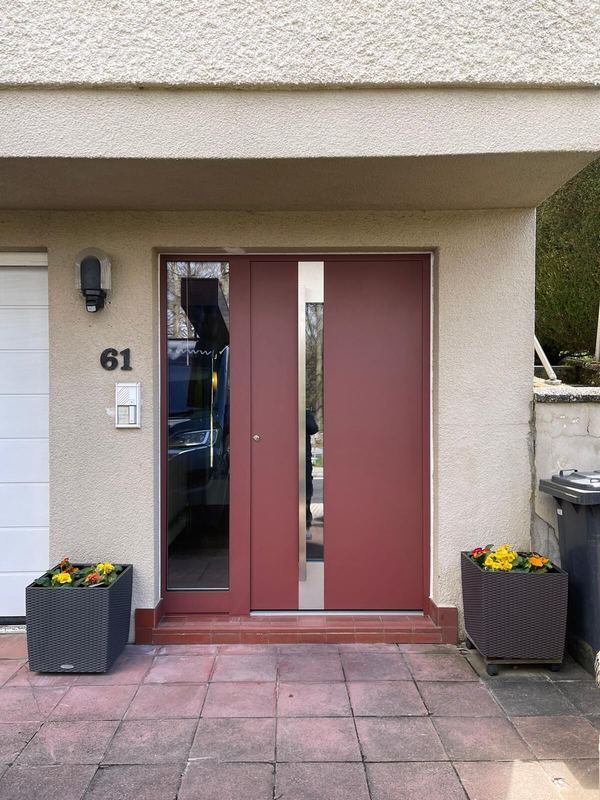 Weinrote Haustür mit verglastem Seitenteil und mittigem Edelstahlband, Blumenkübel neben dem Eingang