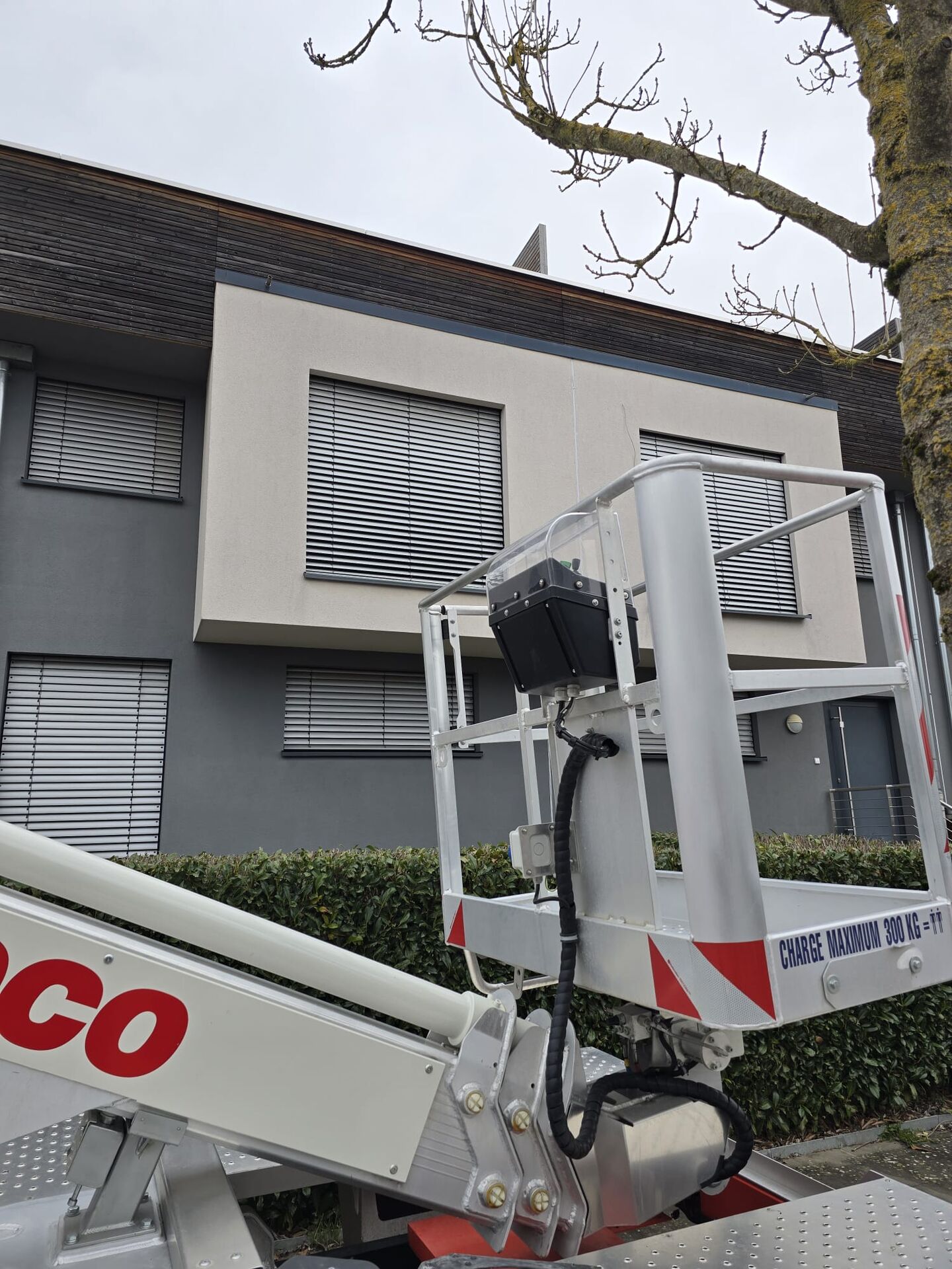 Grey external venetian blinds on a modern façade, aerial work platform in front