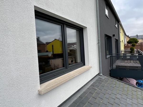 Zweiflügeliges anthrazitfarbenes Fenster mit heller Steinfensterbank in weißer Putzfassade, Seitenansicht