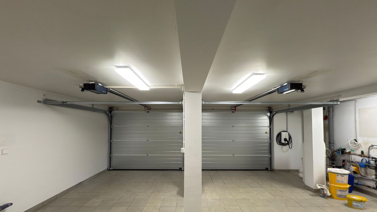 Inside a double garage: two silver sectional doors with ceiling-mounted openers