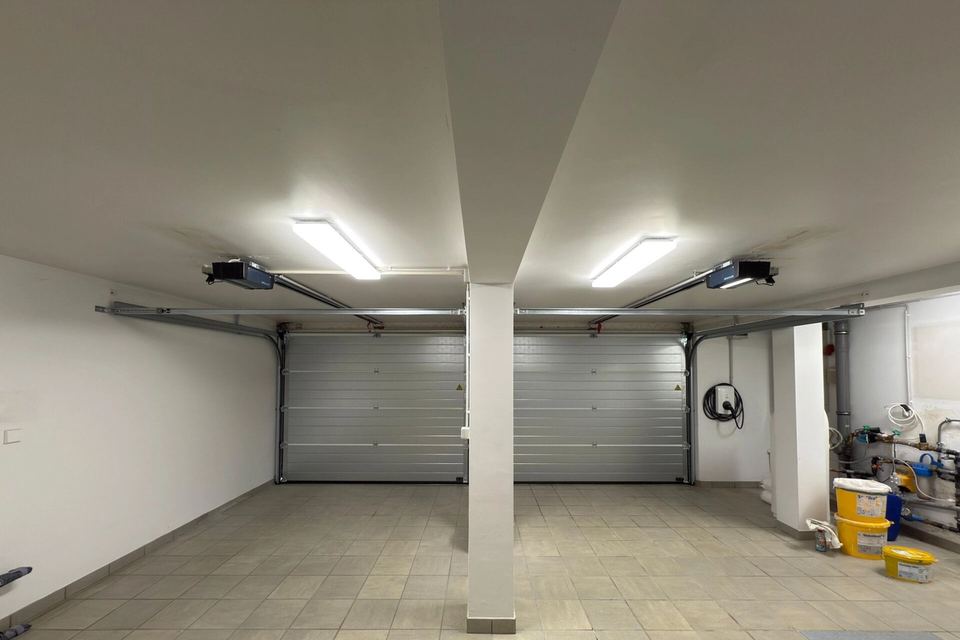 Inside a double garage: two silver sectional doors with ceiling-mounted openers