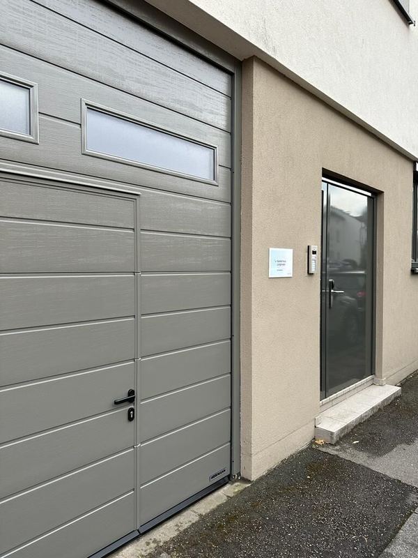Seitenansicht eines grauen Sektionaltors mit Schlupftür und Milchglas neben einer verglasten Haustür