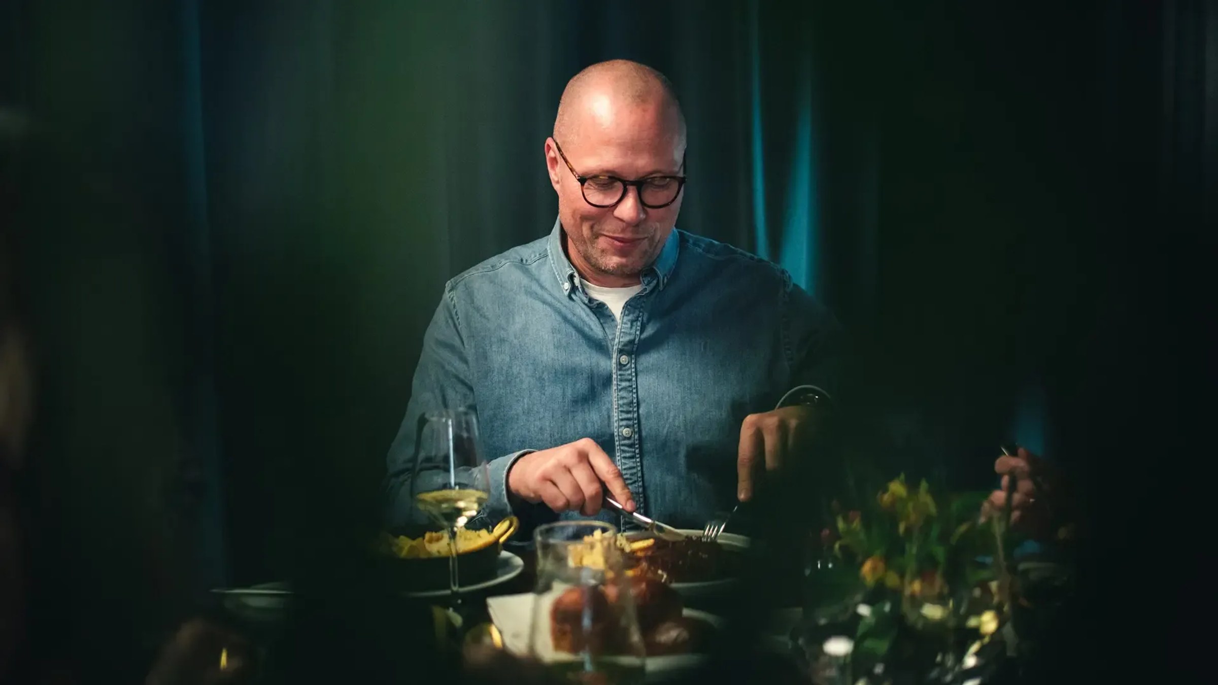 En gjest spiser ved et bord i dempet, grønt lys.