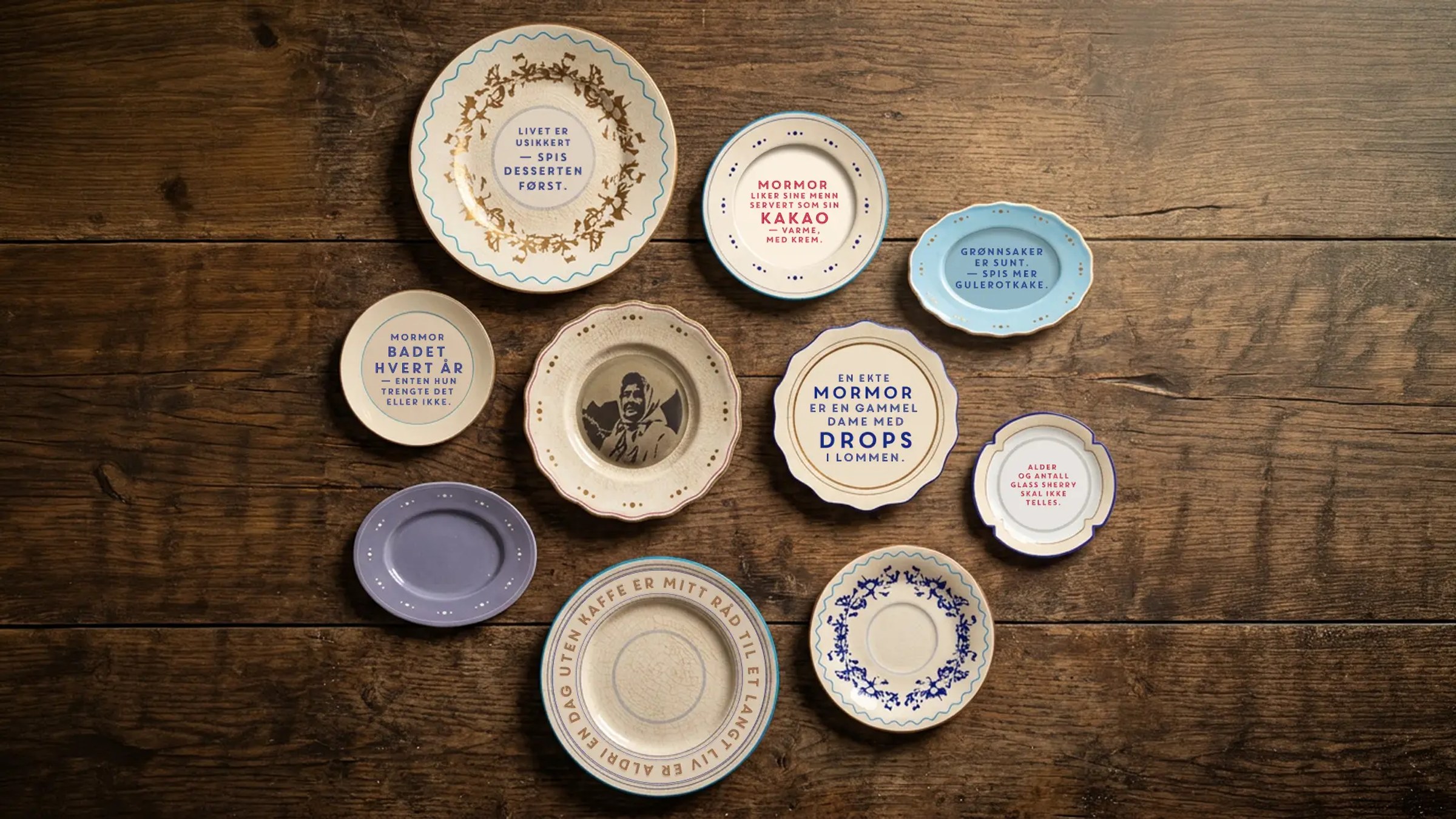 Et utvalg av vintage porselenstallerkener med ulike sitater om «mormor» plassert på et mørkt trebord.