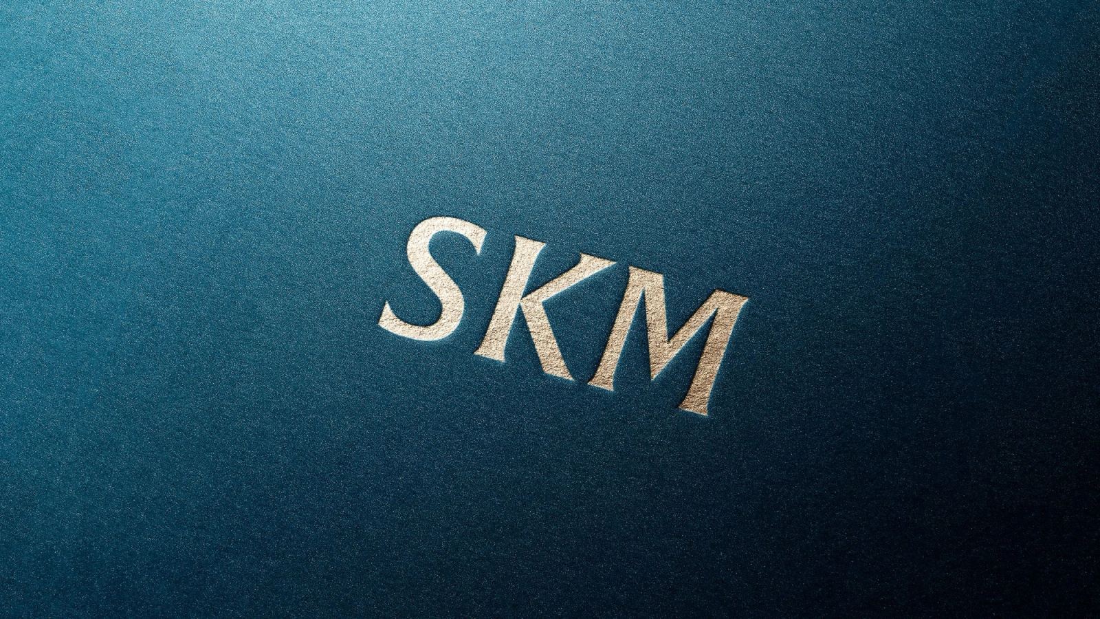 Forkortet SKM-logo i preget folie på blått papir for Sivil klareringsmyndighet.