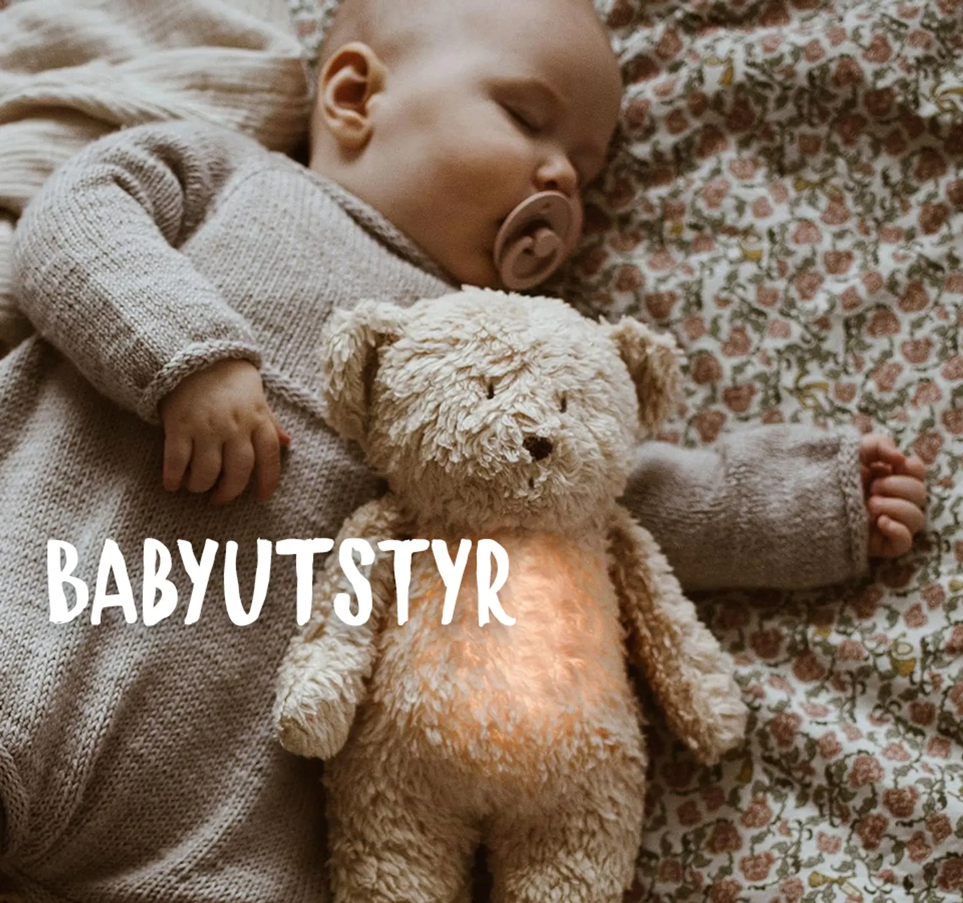 Fotografi av en sovende baby med en Moonie bamse i hendene. Bestselger - hjelper barnet å sove, 839 kr.