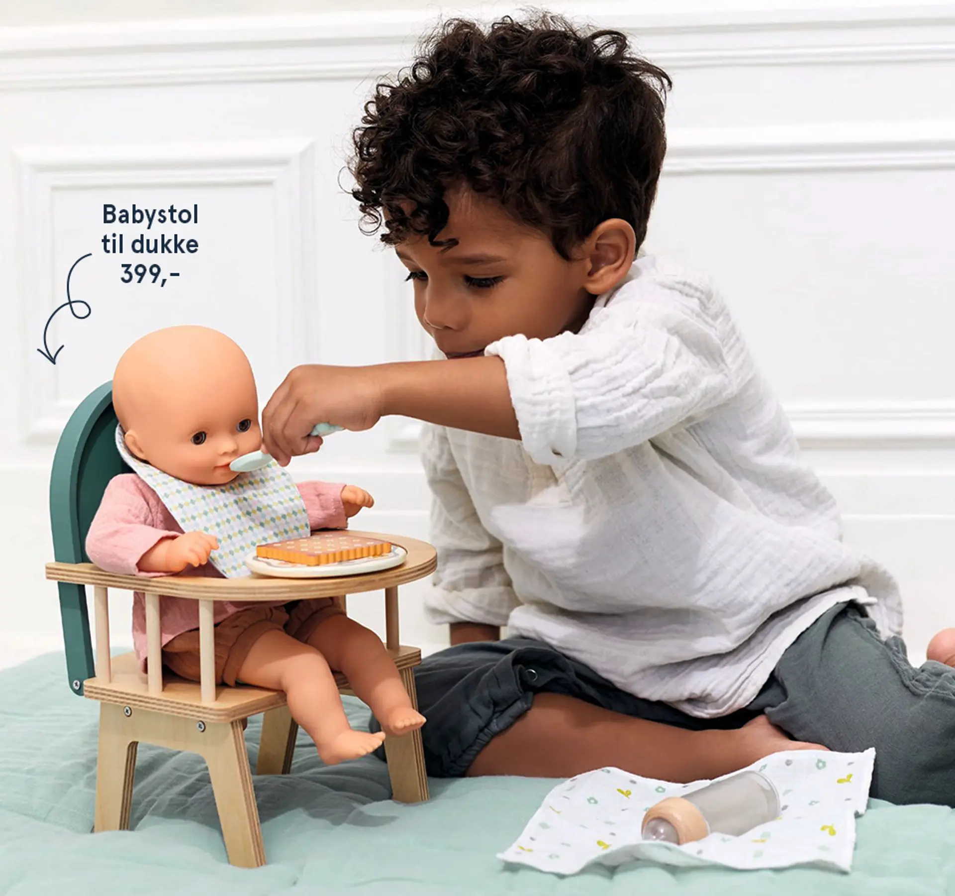 Fotografi av en gutt som leker med en dukke i en babystol for dukke, 399 kr.