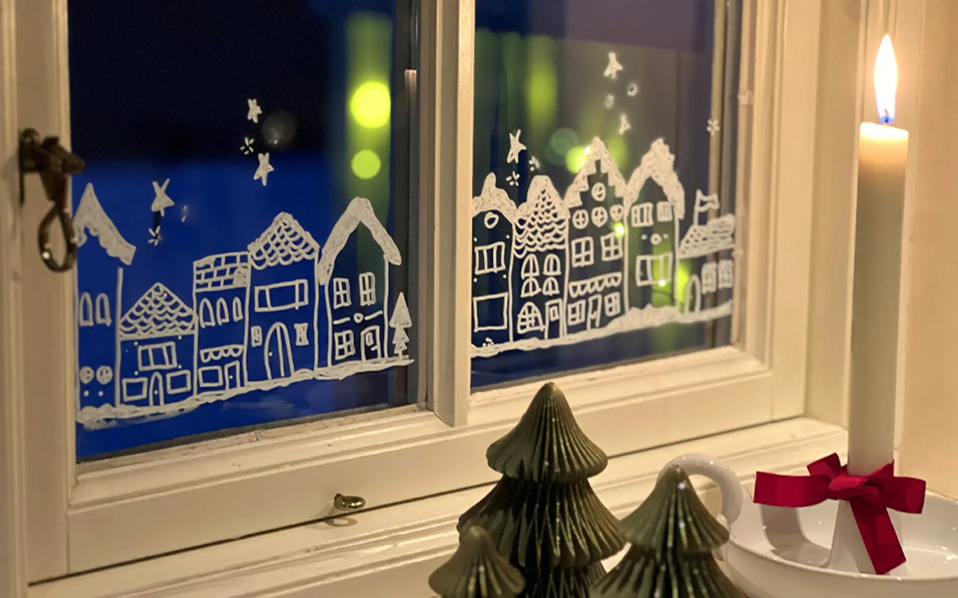 Fotografi av et vindu med julelandsbyen tegnet på med vindustusj.
