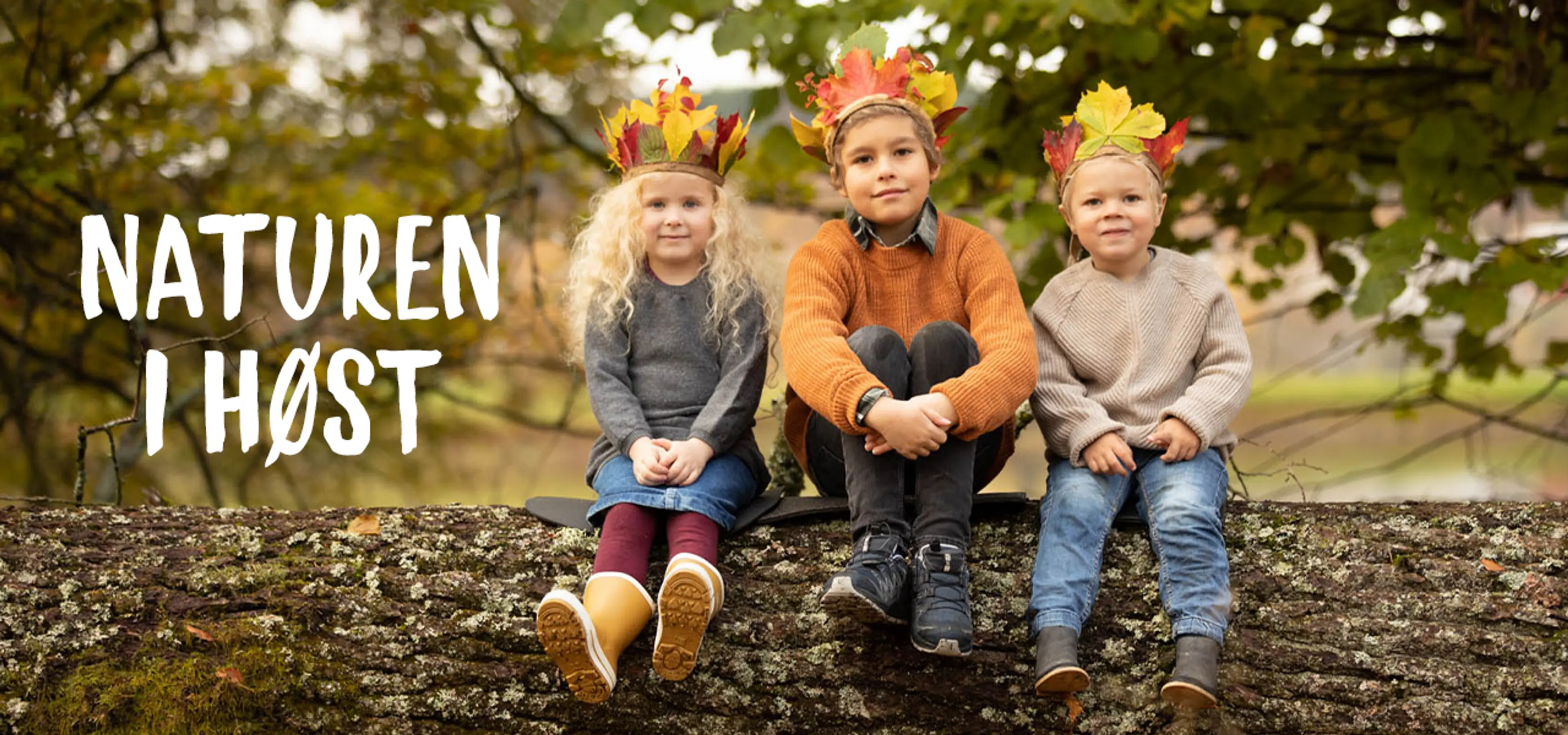 Naturen i høst. Fotografi av barn sittende på en tømmerstokk med høstkroner på hodet.