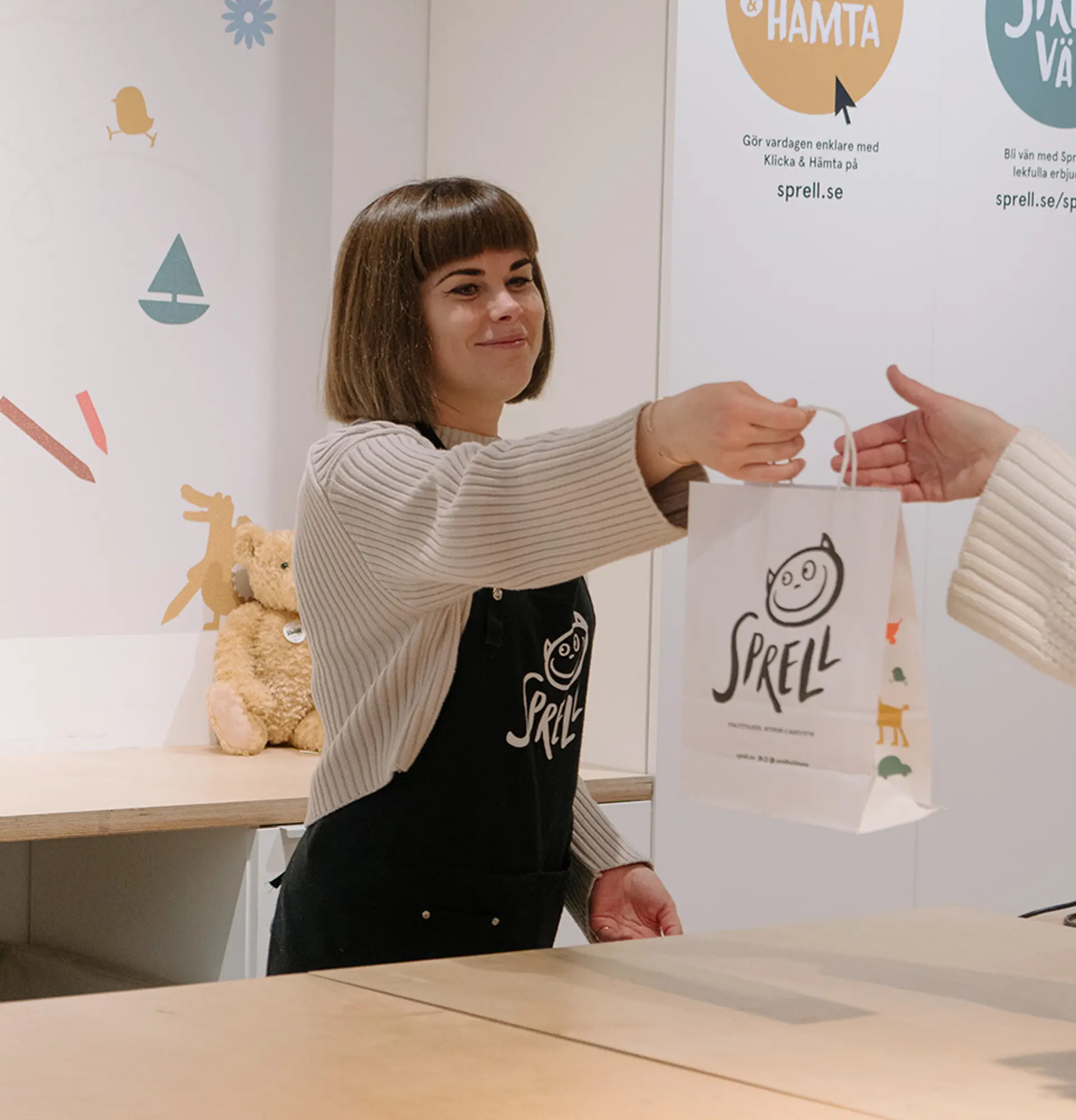 Fotografi av butikkansatt som gir pose til en kunde.