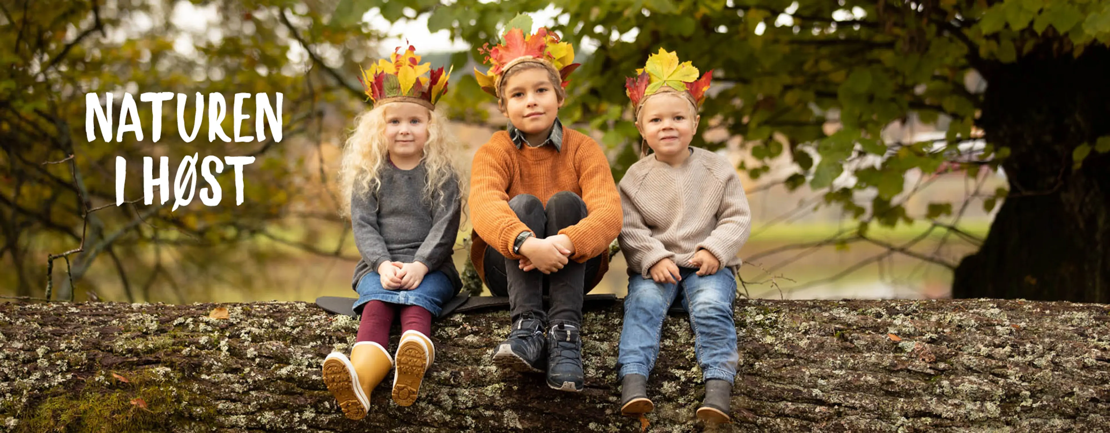 Naturen i høst. Fotografi av barn sittende på en tømmerstokk med høstkroner på hodet.