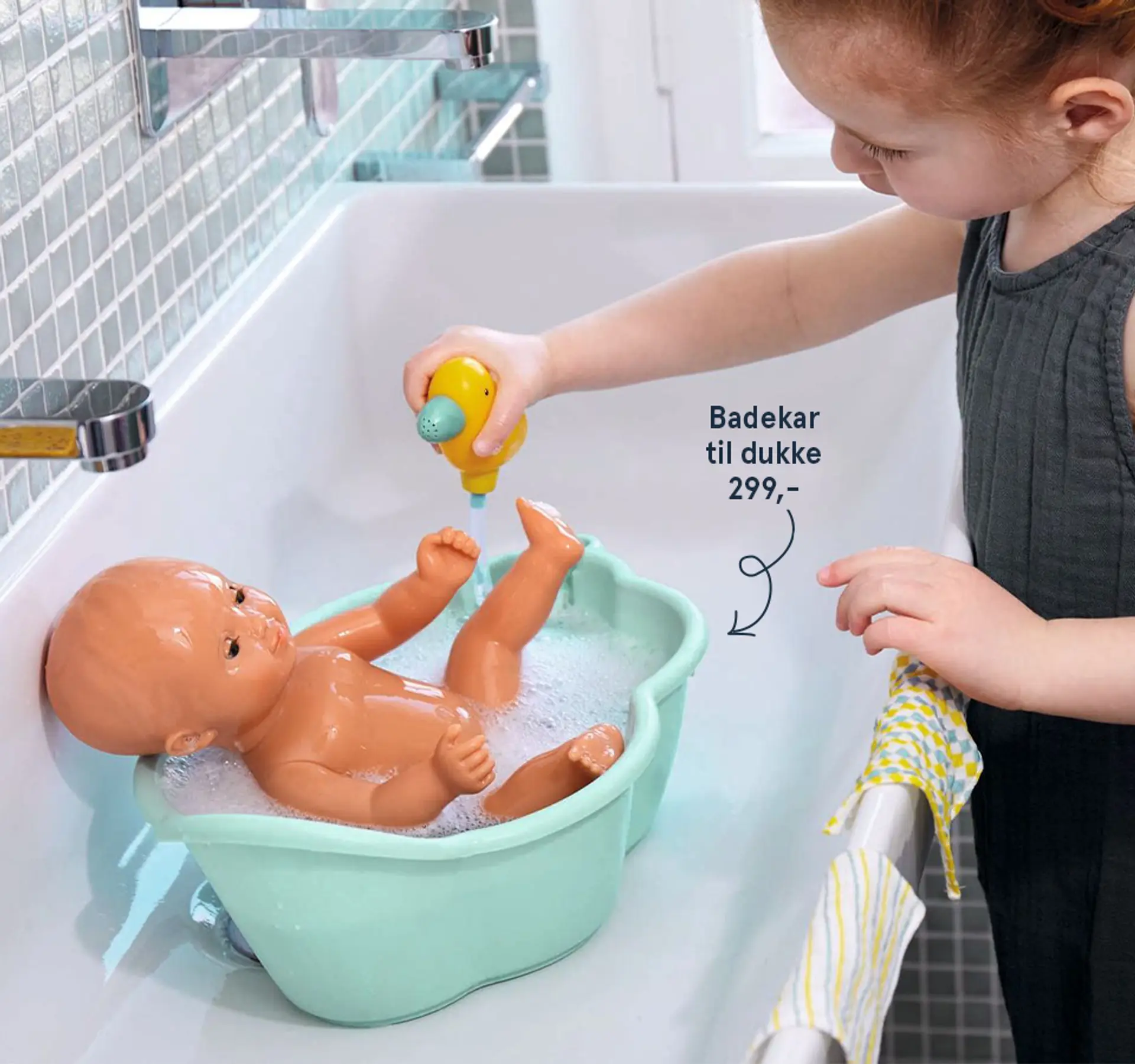 Fotografi av en jente som leker med en dukke i et badekar for dukke, 299 kr.