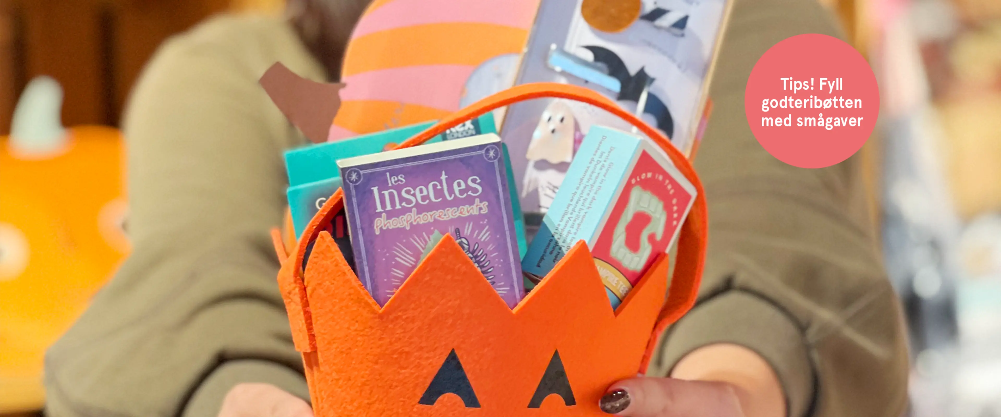 Tips! Fyll godteribøtten med smågaver. Fotogradi av butikkansatt som holder en Halloweenbøtte med håndplukkede smågaver.