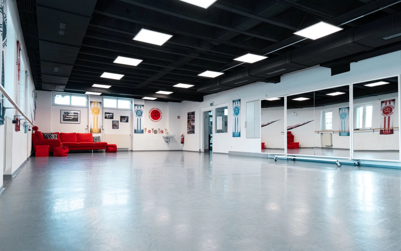 Light Floor in Mödling: großer Saal mit hellgrauem Tanzboden, Spiegelwand und rotem Sofa