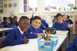 Learners at Queens Church of England Academy writing and smiling at the camera.