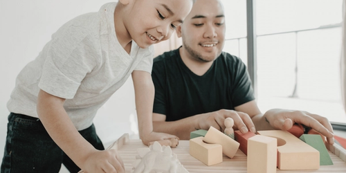 A child and a parent improving confidence using building blocks and toy dinosaurs.