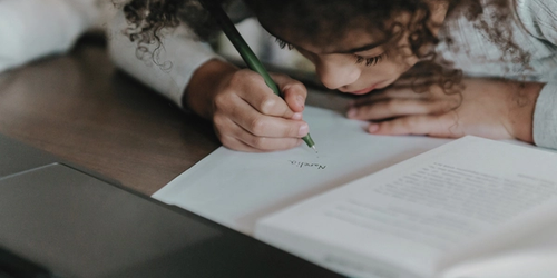 A student combining writing instruction with reading while doing their homework, facing a laptop.