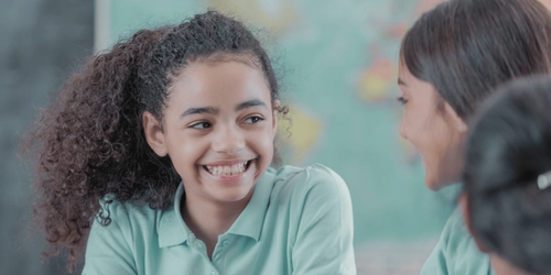 A learner smiling and her friends in the classroom.