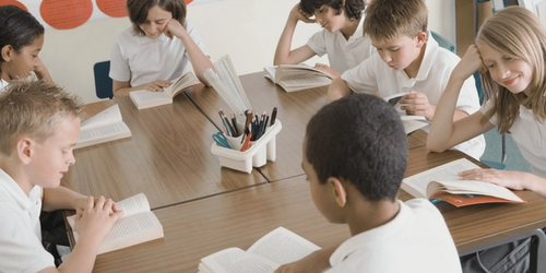Students around a table reading a book.