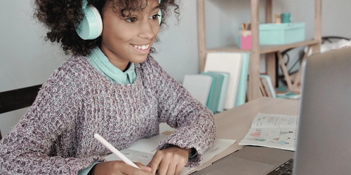 A learner making good homework habits and doing their homework using a laptop, wearing headphones.