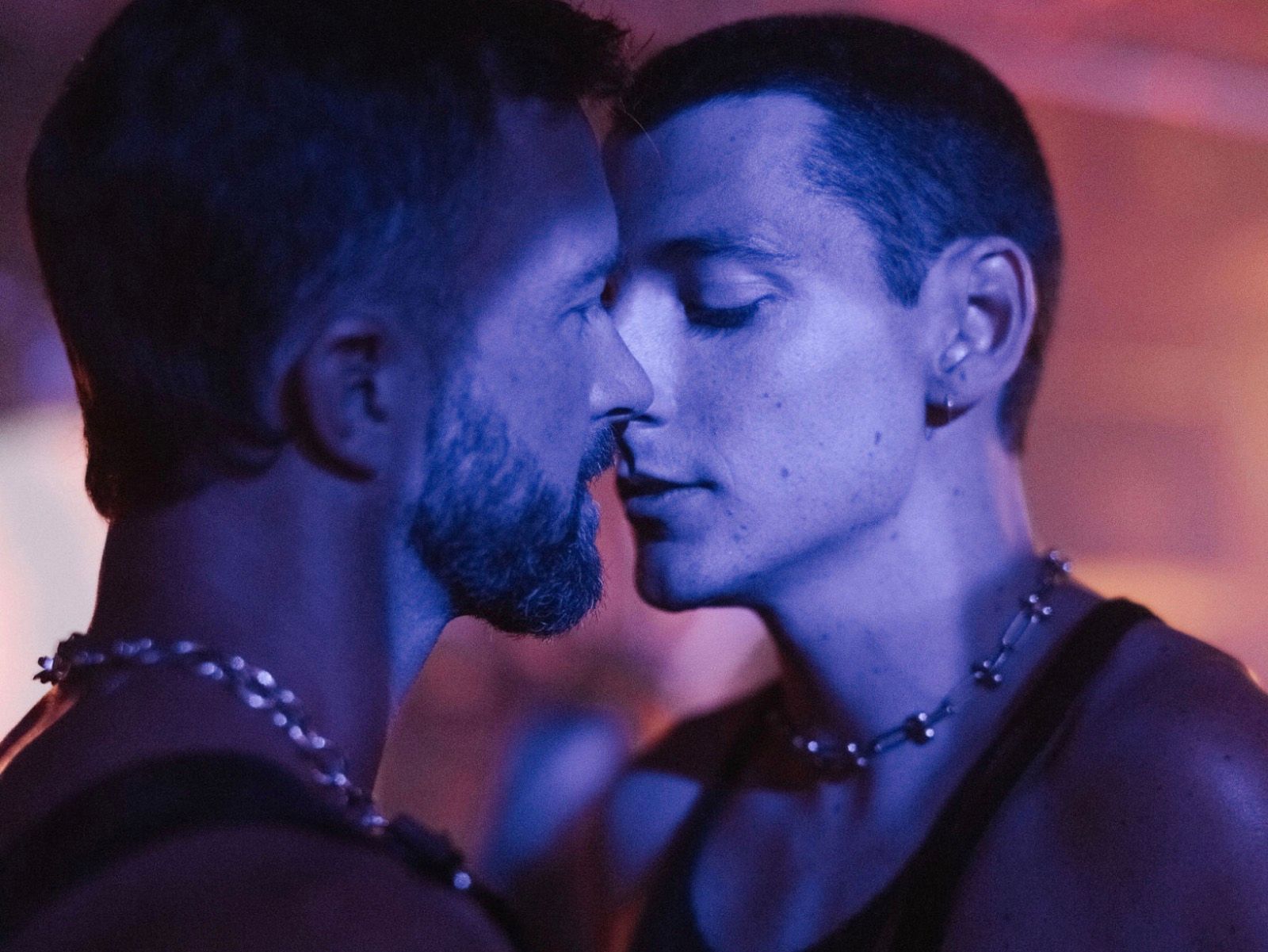 Two men kiss in blue light.