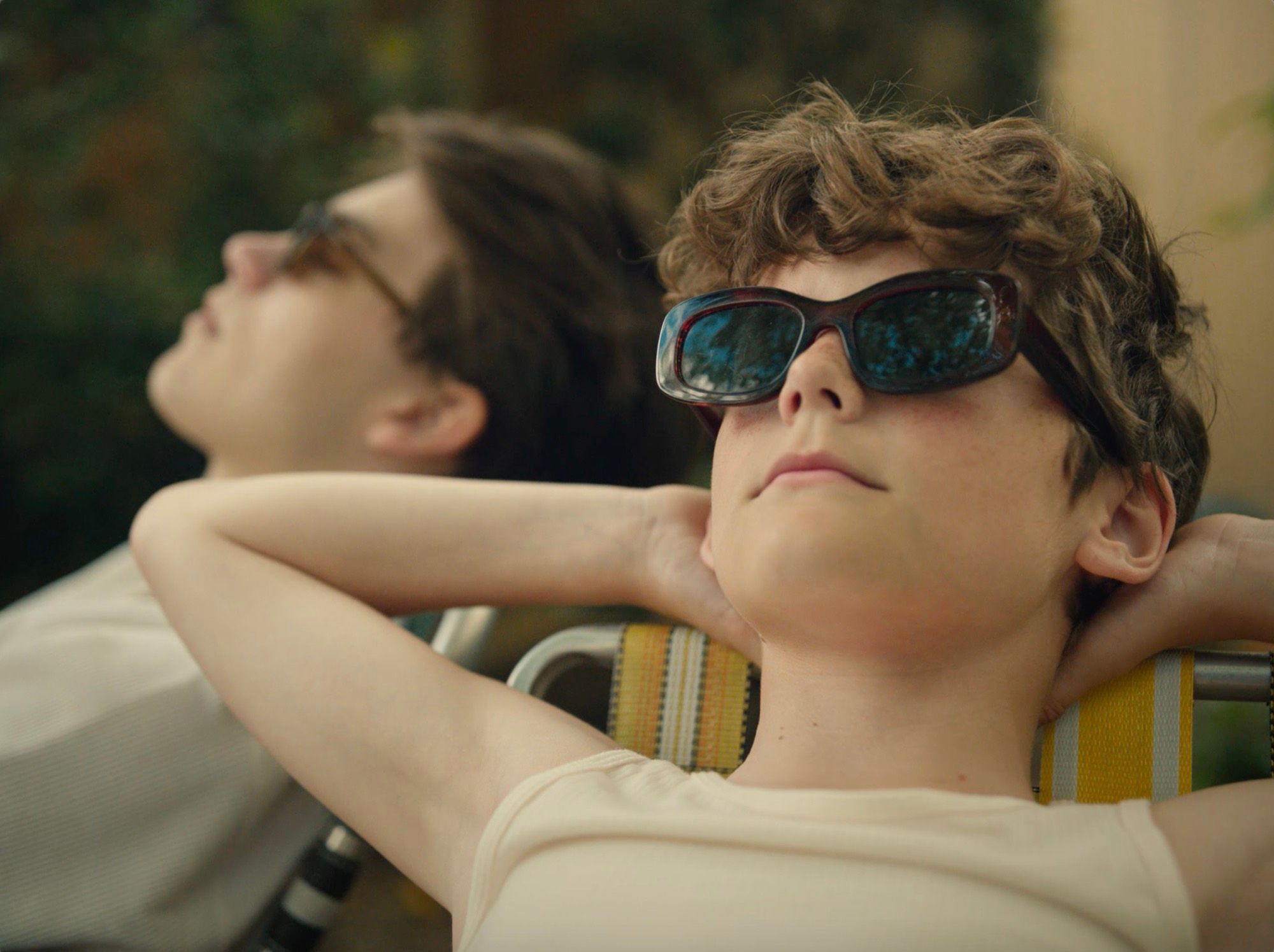 A boy in sunglasses lies back in the sun.