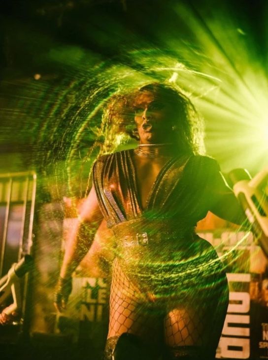 Behind the scenes: a drag performer on stage in a burst of green light.