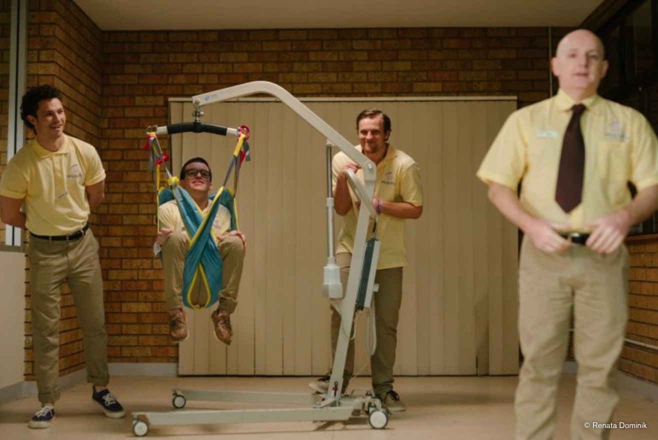 A man in a patient hoist, carers looking on.