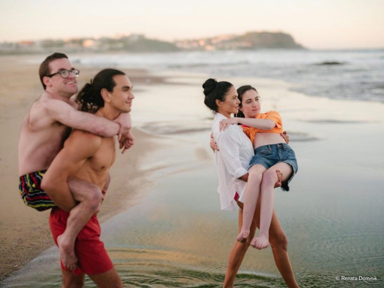 Two couples carry each other at the beach at dusk.