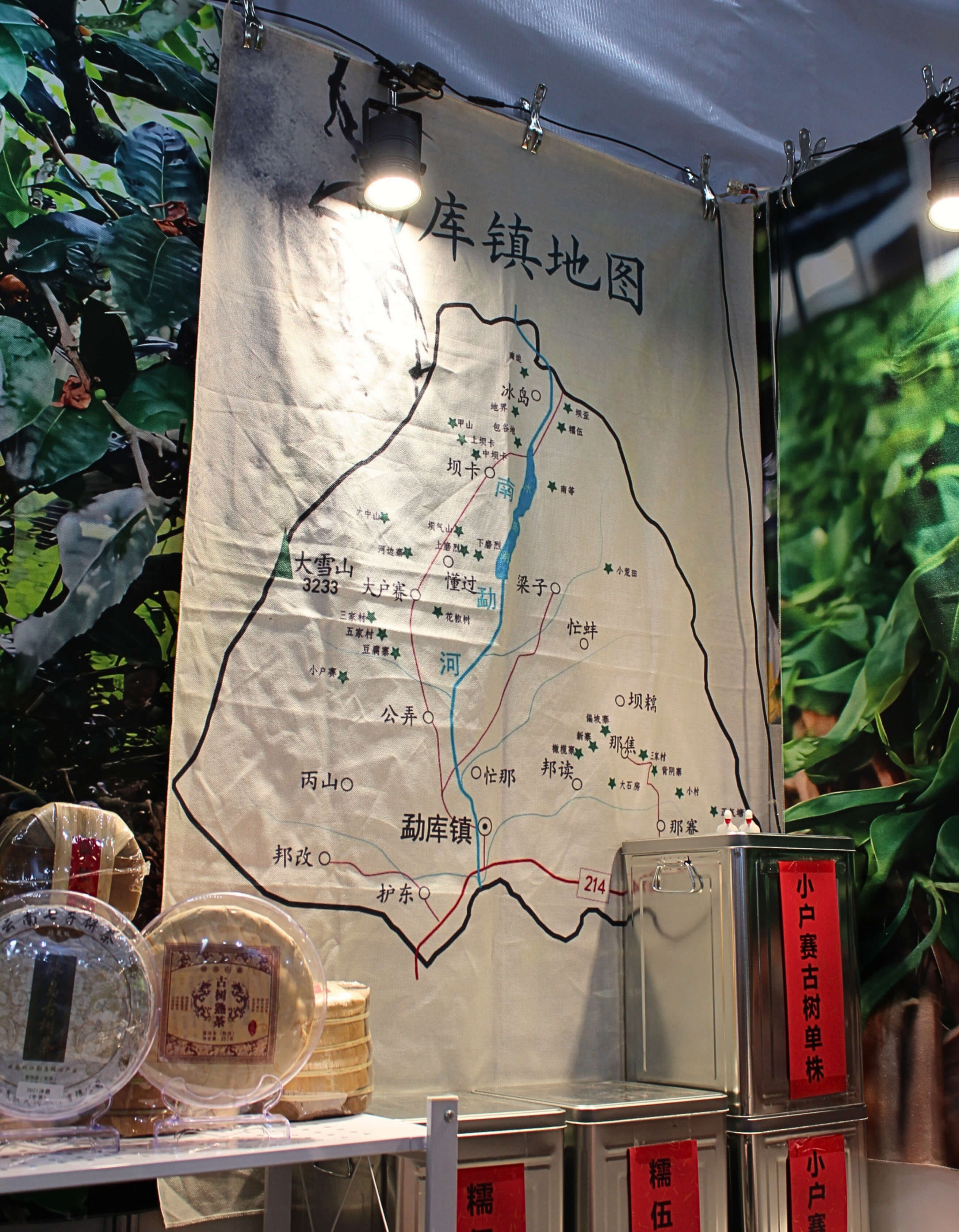 A map of Mengku town in Lincang, Yunnan, hanging at the back of Fu Yuanyuan’s stand. Villages are marked along the Nanmeng river valley, with Mengku town at the southern end and Bingdao at the northern end. Tins of tea sit on shelves beneath it.