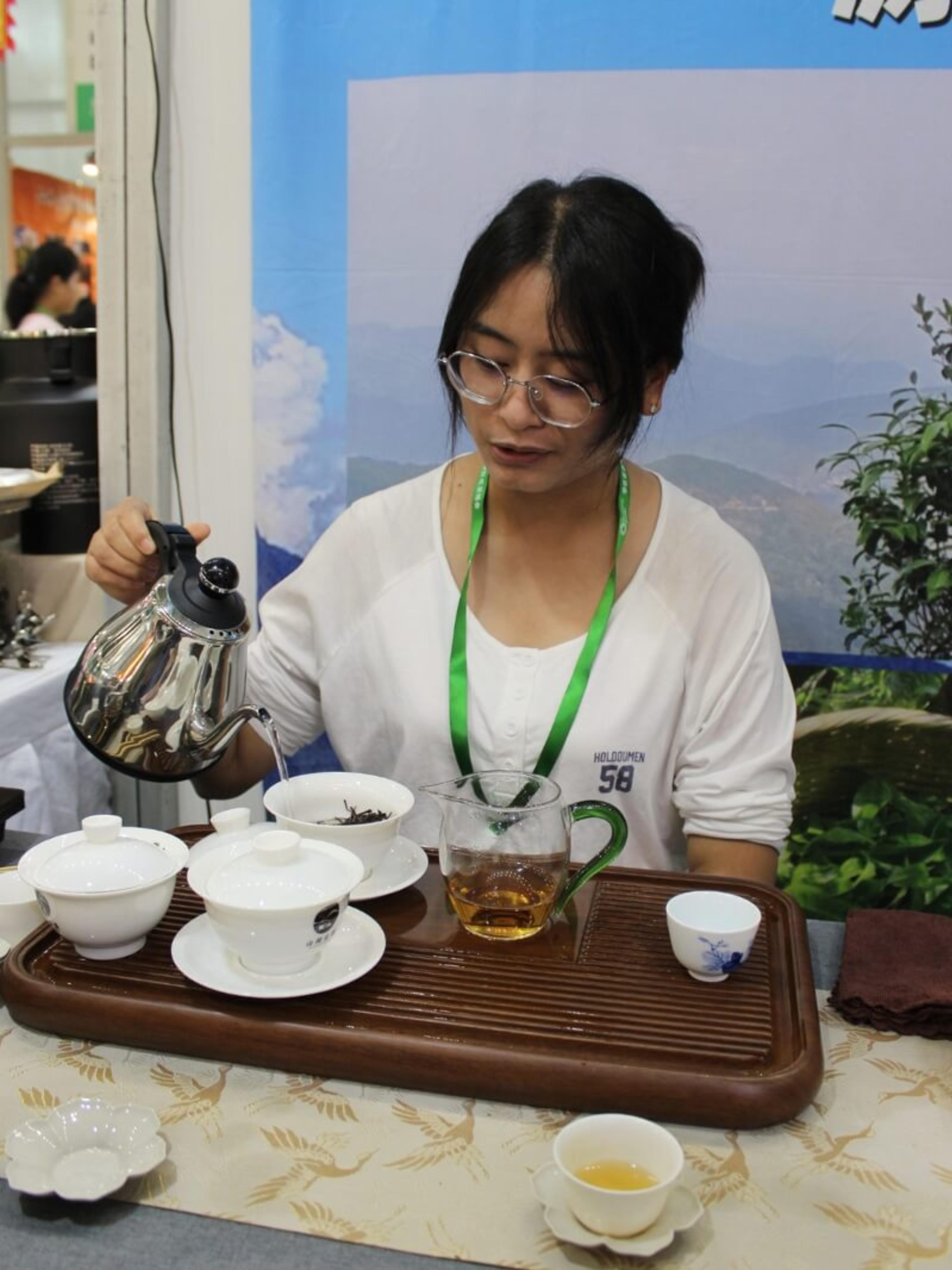A woman pours from a kettle into a gaiwan at a tasting table.