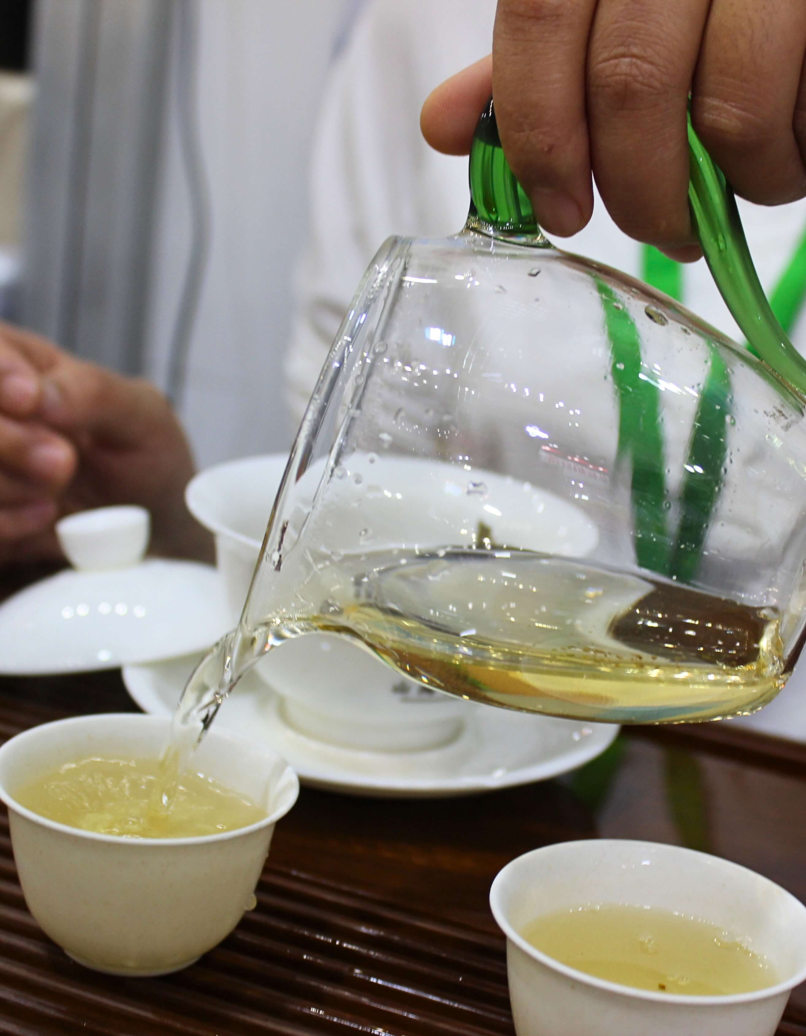 Pouring brewed puer from a fairness pitcher into white tea cups.