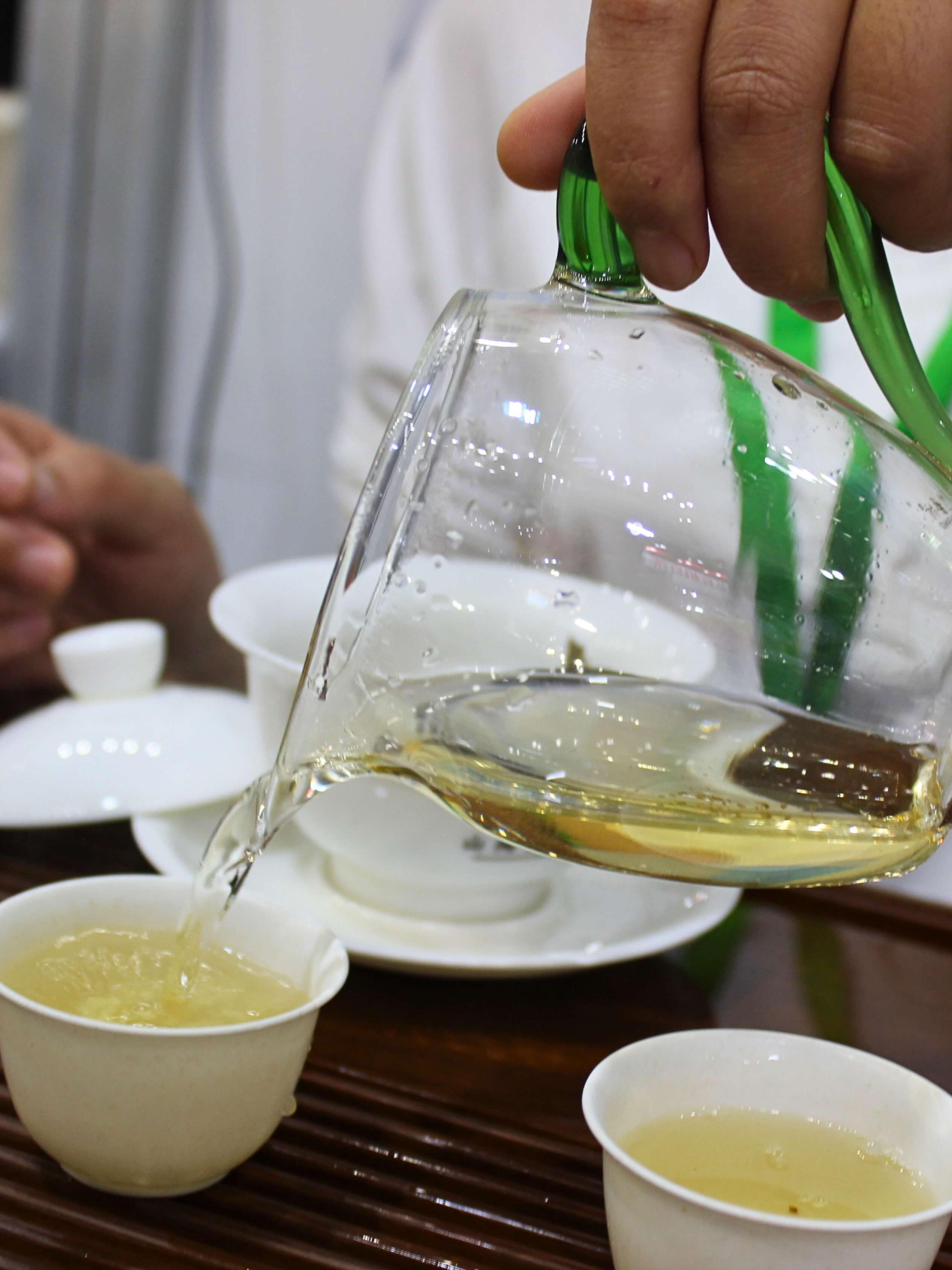 Pouring brewed puer from a fairness pitcher into white tea cups.
