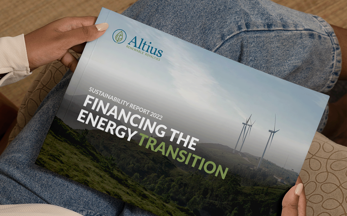 Hand holding a printed Altius Renewable Royalties sustainability report with a wind turbine photo and the headline 'Financing the Energy Transition.'