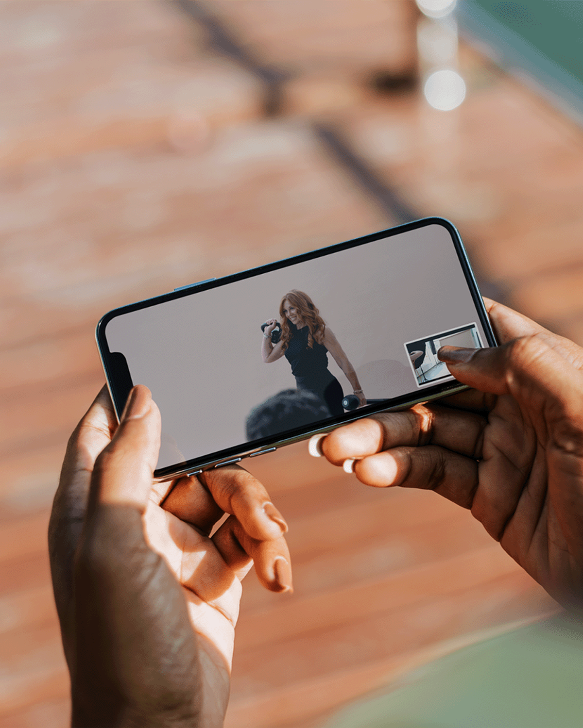 Alt text: "Hand holding a phone horizontally, displaying a video of an instructor demonstrating a kettlebell exercise for an online pilates class.