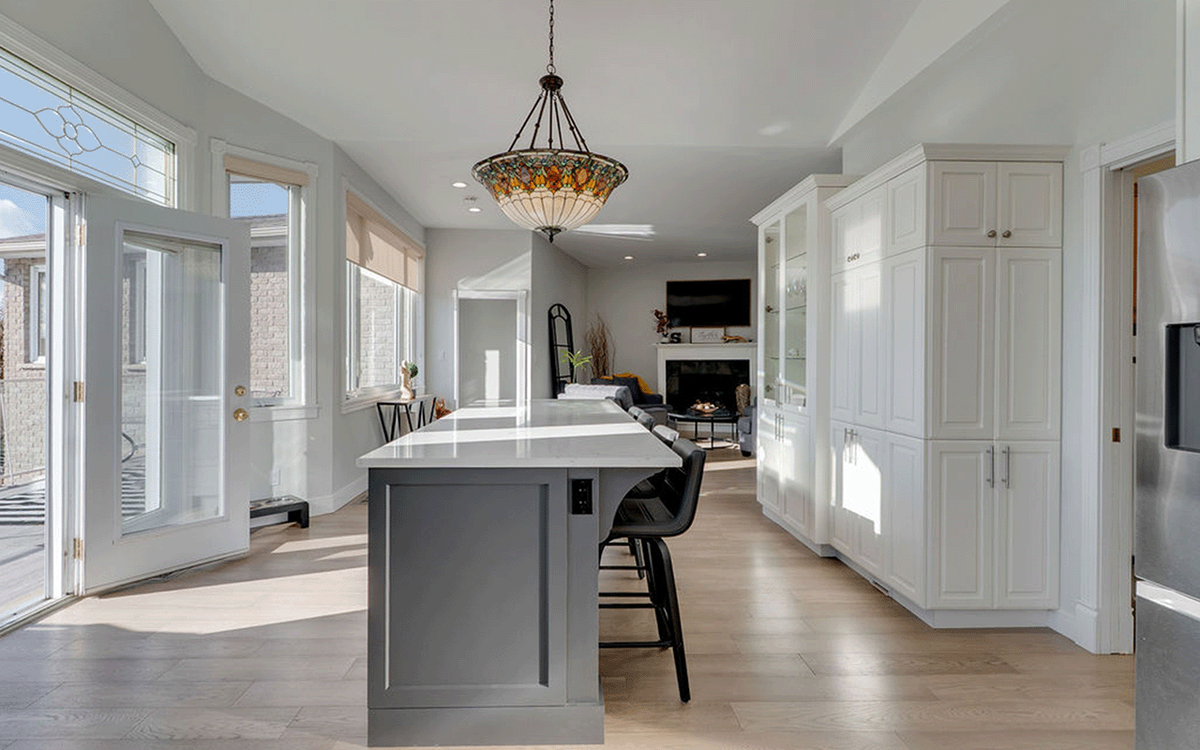 Bright open-concept kitchen with a grey island, white cabinetry, and a stained glass pendant light, staged for a real estate listing.