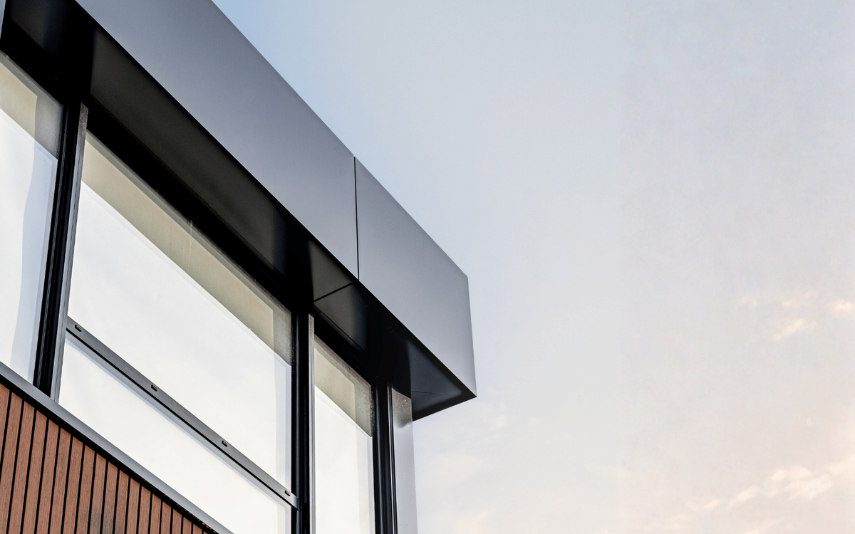 Close-up architectural detail of a modern building's black panel overhang and wood slat siding against a soft sky.
