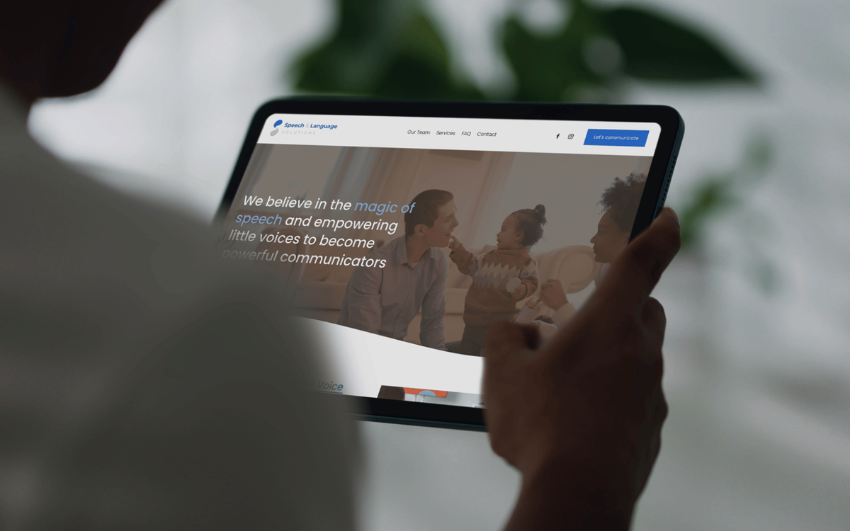 Tablet held by a person, displaying a speech therapy clinic homepage with a family photo and a headline about empowering communication.