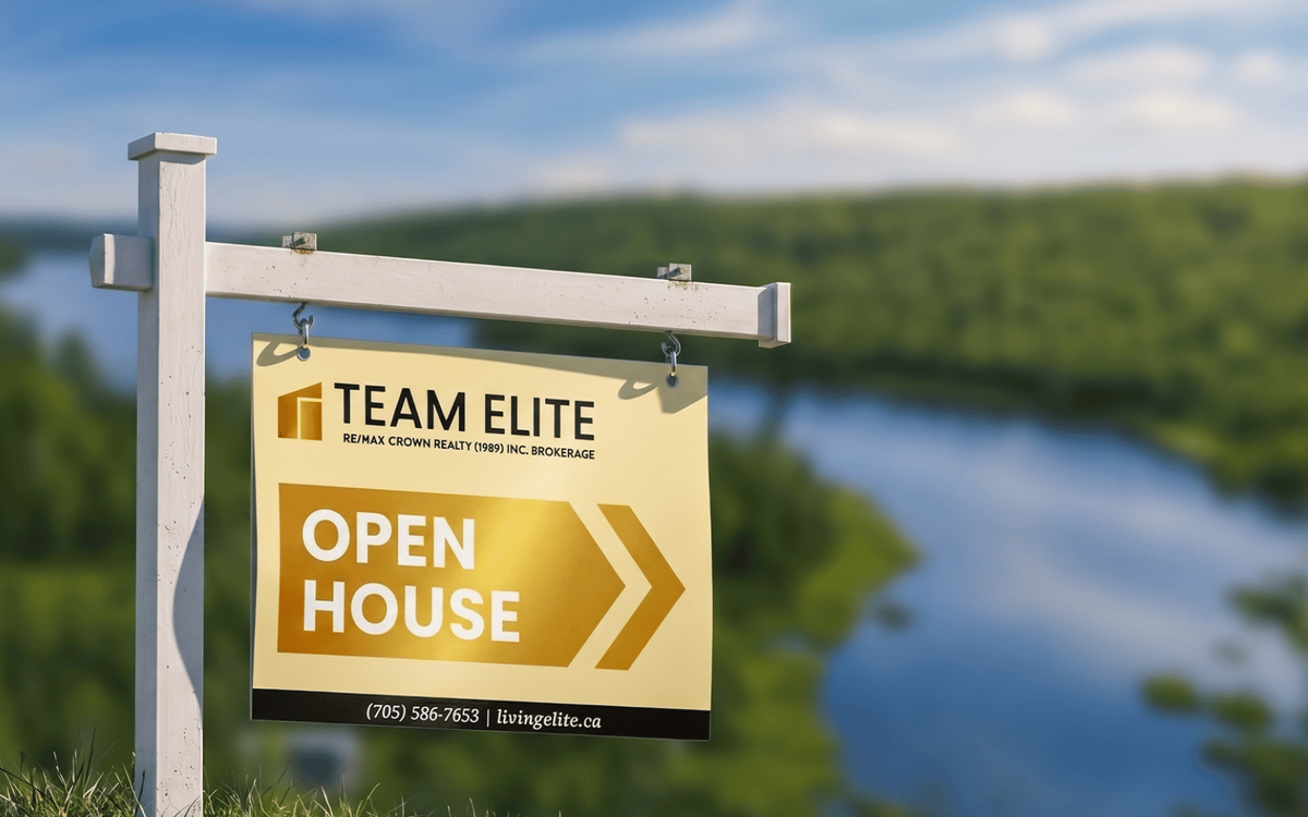 Team Elite real estate open house sign mounted on a post with a lake and forest in the background.