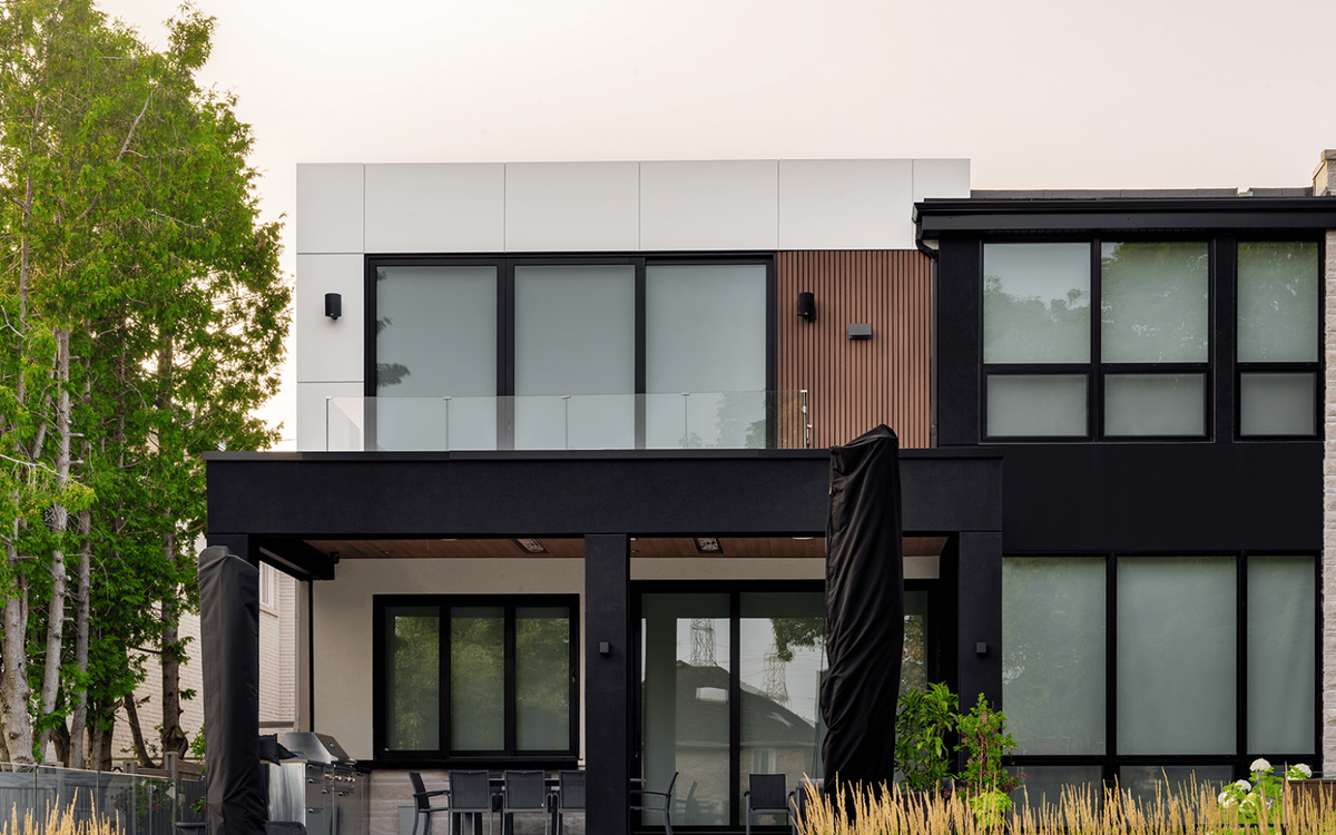 Modern two-story home exterior with black and white panel siding, glass balcony railing, and covered patio, photographed at dusk.