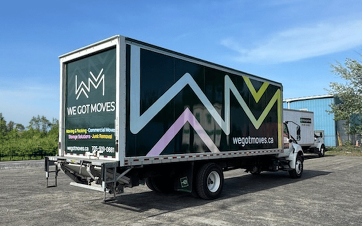The back of a moving truck wrapped in a dark green and geometric design for We Got Moves, with the company logo, services, and website listed.