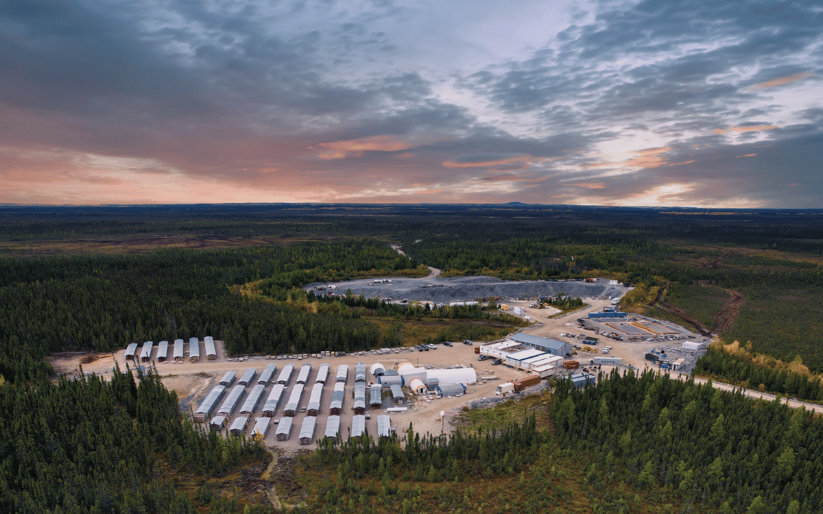 Aerial drone photo of a mining site at dusk, showing rows of storage buildings, processing facilities, and forest surrounding the operation.