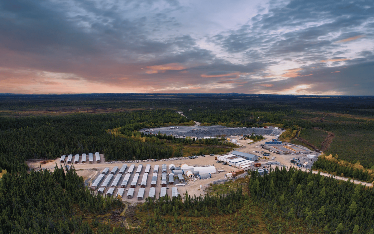 An aerial view of a mining camp at dusk, showing rows of camp trailers and site facilities surrounded by boreal forest.