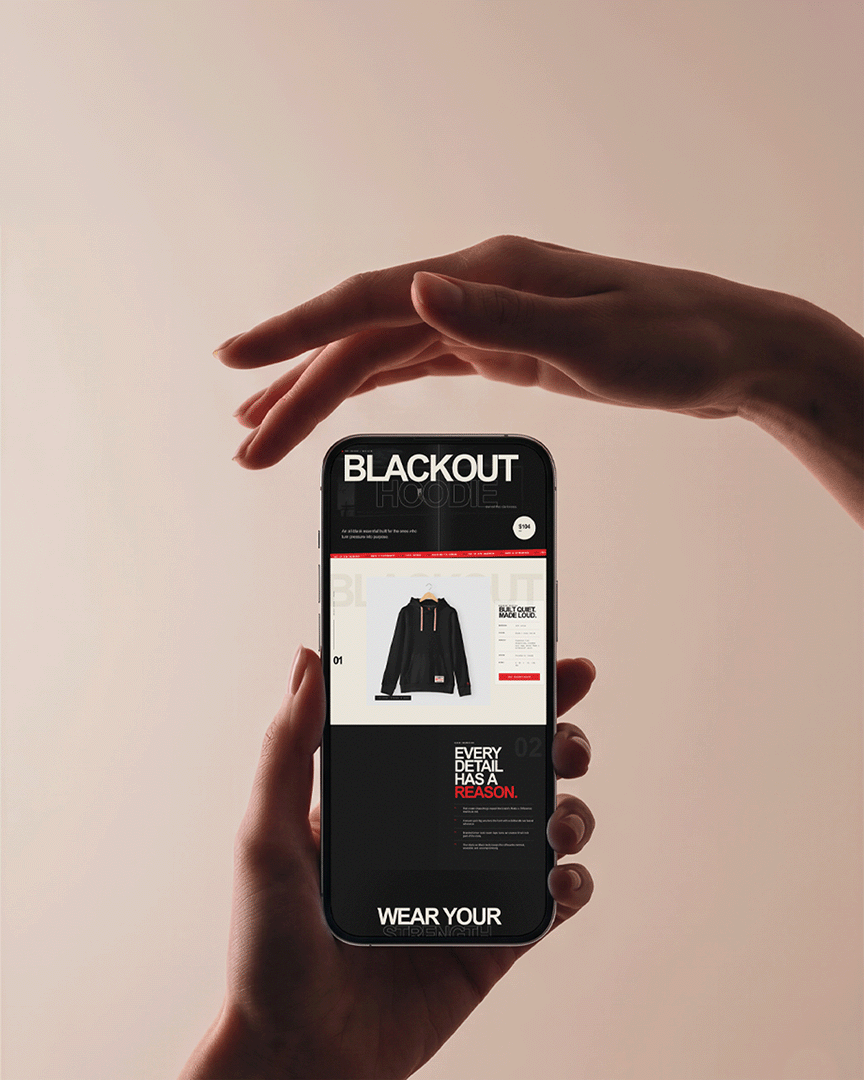 Hand holding a phone displaying a MAD Apparel product page for the Blackout Hoodie, featuring a black hoodie photo, pricing, and brand messaging.