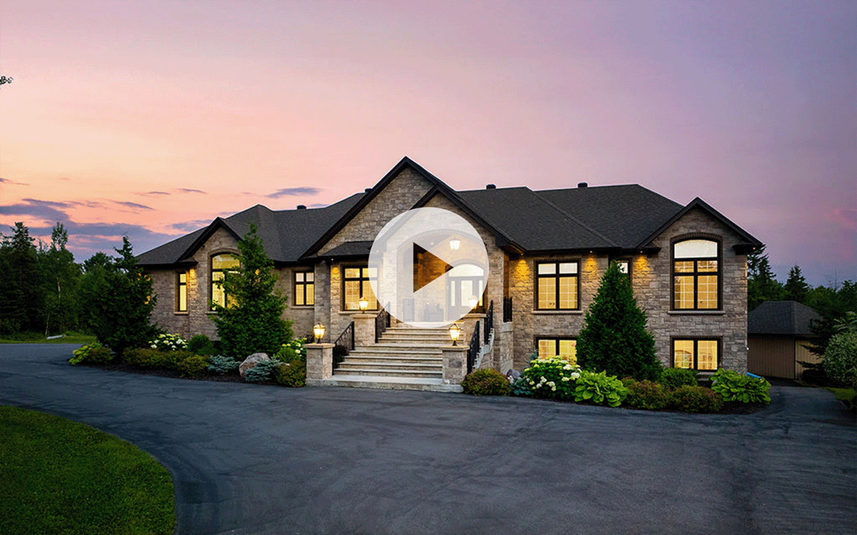Video thumbnail of a large stone bungalow exterior at dusk, with lit windows and a curved driveway, for a real estate listing.