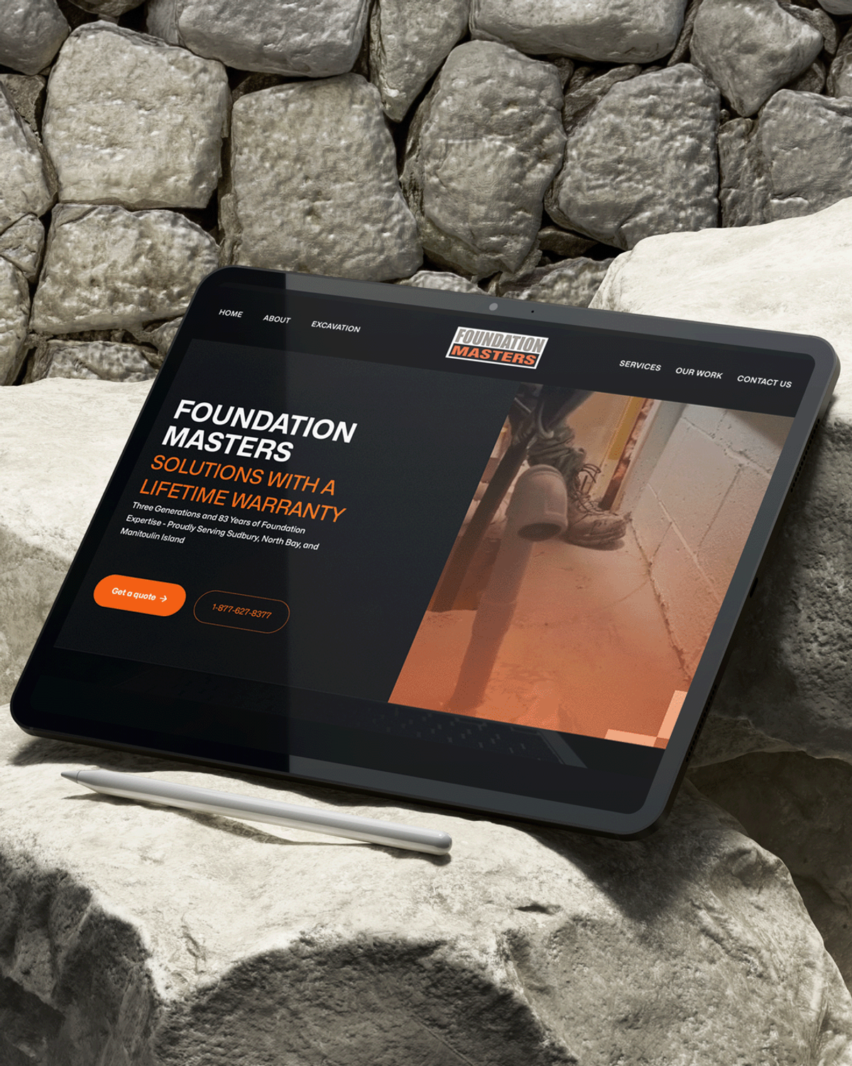 Tablet displaying the Foundation Masters website homepage with a headline about lifetime warranty foundation repair, resting on a stone wall.