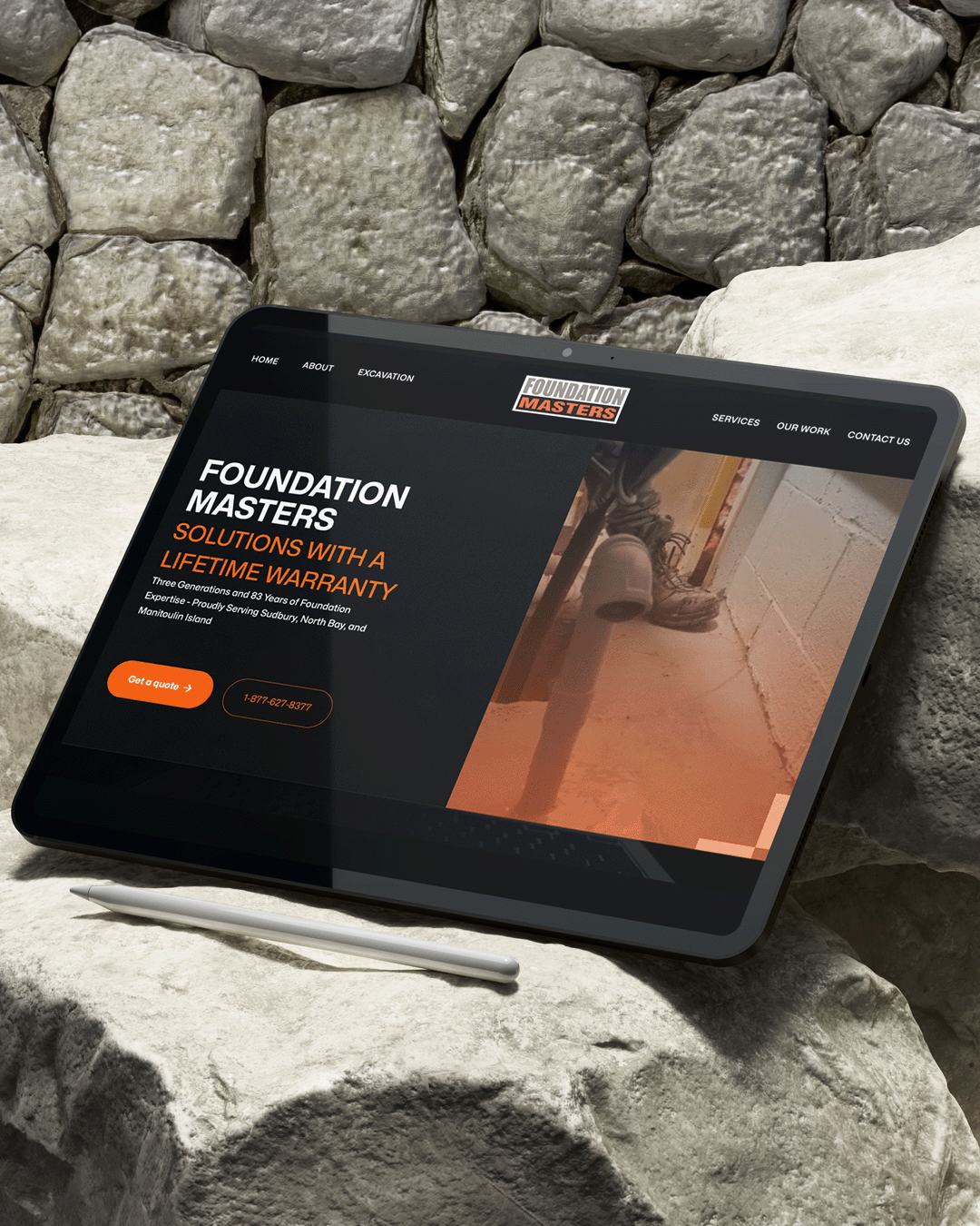Tablet displaying the Foundation Masters website homepage with a headline about lifetime warranty foundation repair, resting on a stone wall.