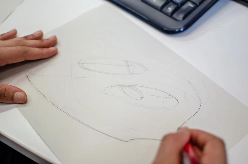 two hands on a page of A4, the right holding a pen and roughly sketching a clothes iron